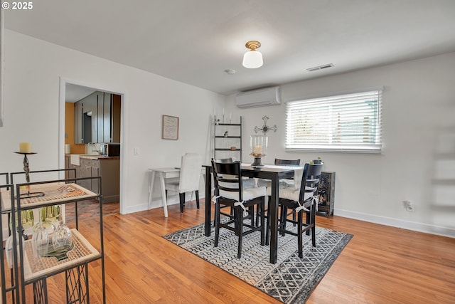 dining room featuring baseboards, visible vents, a wall unit AC, and light wood-style floors