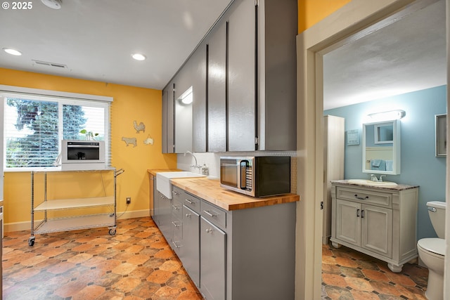 kitchen featuring a sink, visible vents, butcher block countertops, stainless steel microwave, and gray cabinetry