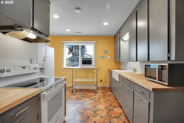 kitchen featuring white electric range oven, a sink, wooden counters, stainless steel microwave, and baseboards