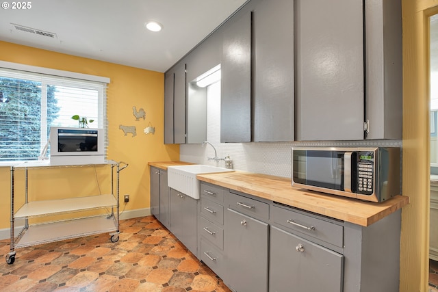 kitchen with a sink, baseboards, stainless steel microwave, gray cabinetry, and butcher block counters
