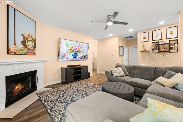 living room featuring a ceiling fan, wood finished floors, baseboards, a tiled fireplace, and recessed lighting