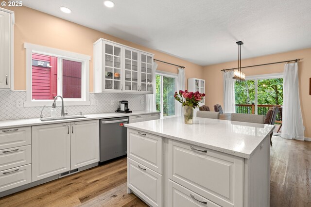 kitchen with dishwasher, a sink, light wood finished floors, white cabinets, and a chandelier