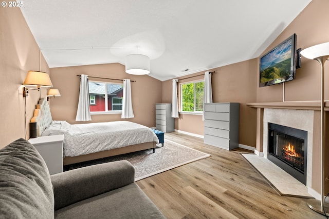 bedroom featuring lofted ceiling, a fireplace, wood finished floors, and baseboards