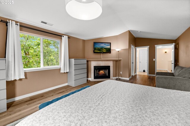 bedroom with wood finished floors, baseboards, vaulted ceiling, and a tile fireplace