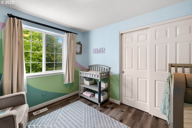 bedroom with a textured ceiling, dark wood-type flooring, baseboards, and a closet