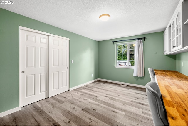 unfurnished bedroom featuring wood finished floors, a textured ceiling, a closet, baseboards, and a desk