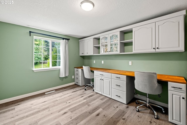 office space with built in desk, light wood-style flooring, baseboards, and a textured ceiling