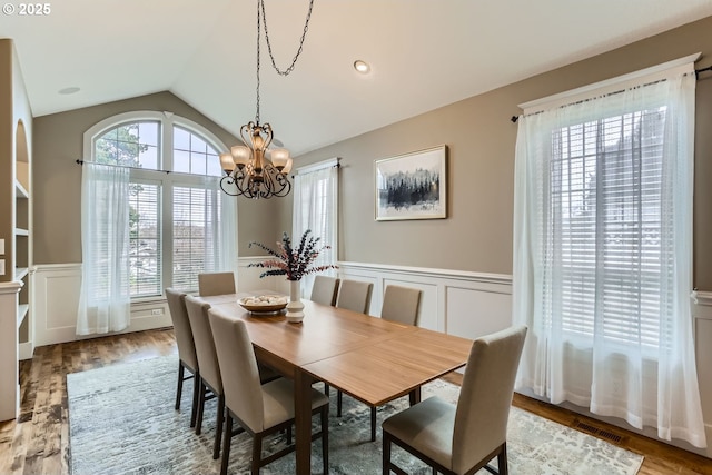 dining room featuring lofted ceiling, a notable chandelier, wood finished floors, and wainscoting