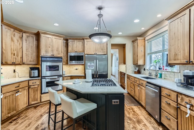 kitchen featuring light wood-style flooring, stainless steel appliances, a sink, a center island, and tasteful backsplash