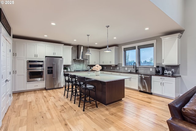 kitchen featuring a kitchen bar, appliances with stainless steel finishes, wall chimney range hood, pendant lighting, and a center island