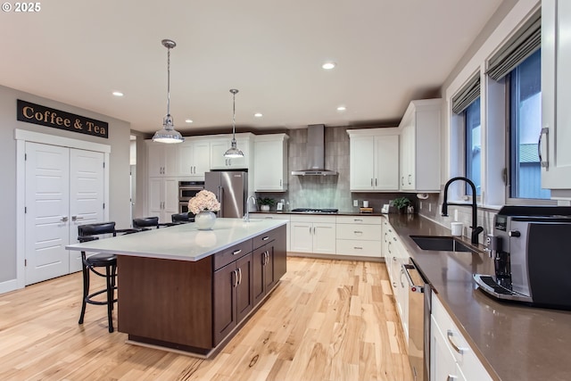 kitchen featuring sink, wall chimney exhaust hood, backsplash, a kitchen island, and appliances with stainless steel finishes