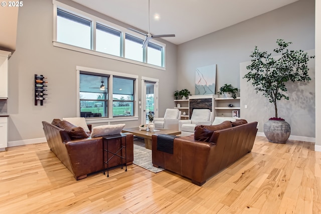 living room featuring ceiling fan, light hardwood / wood-style floors, a fireplace, and a high ceiling