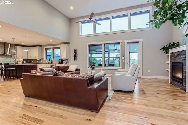 living room with ceiling fan, a high ceiling, light hardwood / wood-style flooring, plenty of natural light, and a fireplace