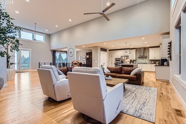 living room with ceiling fan, light hardwood / wood-style floors, and a towering ceiling