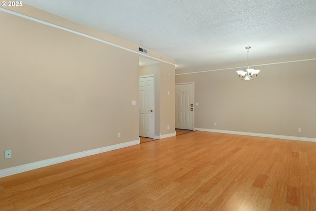 spare room featuring a notable chandelier, light hardwood / wood-style flooring, and a textured ceiling