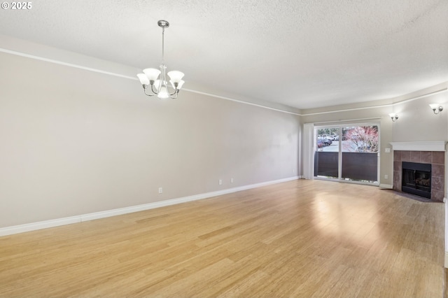 unfurnished living room with baseboards, a tiled fireplace, a textured ceiling, light wood-type flooring, and a chandelier