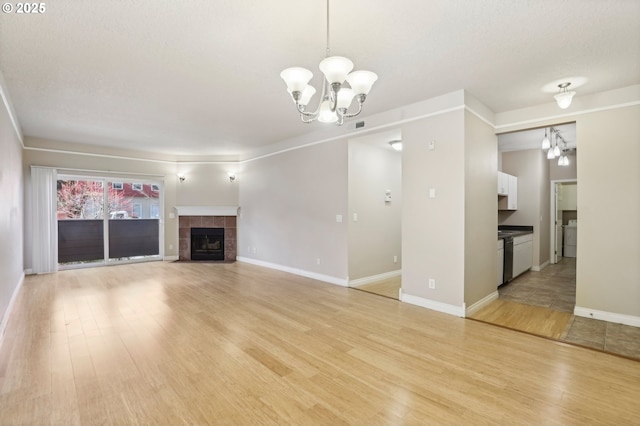 unfurnished living room featuring baseboards, a tiled fireplace, light wood-style flooring, washer / clothes dryer, and a chandelier