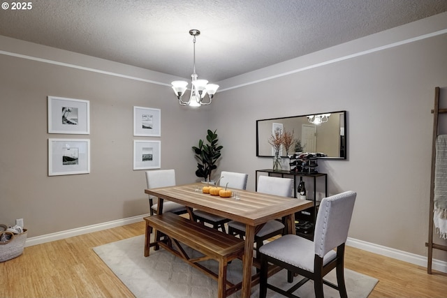 dining area featuring a notable chandelier, a textured ceiling, and light wood-type flooring