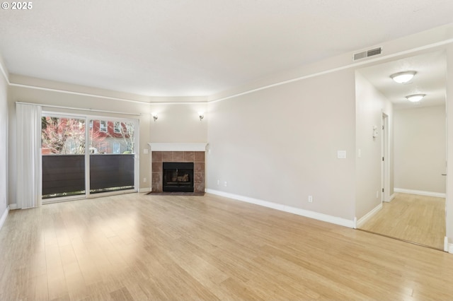 unfurnished living room featuring light wood-type flooring, baseboards, visible vents, and a tiled fireplace