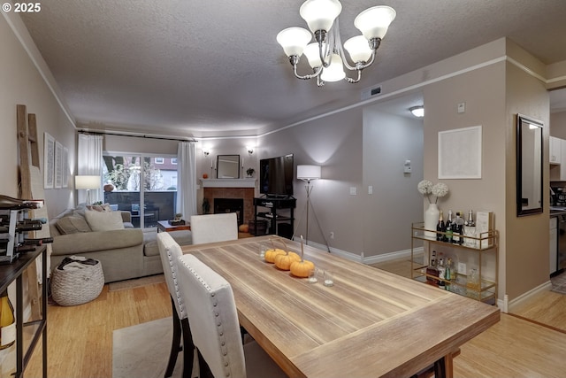 dining area with a tiled fireplace, a notable chandelier, light hardwood / wood-style floors, and a textured ceiling