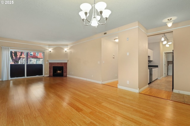 unfurnished living room featuring a tile fireplace, a chandelier, a textured ceiling, and light hardwood / wood-style floors