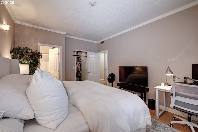 bedroom featuring ornamental molding, a spacious closet, light hardwood / wood-style floors, and a textured ceiling