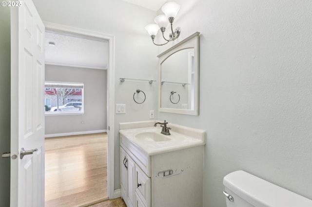 bathroom featuring toilet, vanity, wood finished floors, a chandelier, and baseboards