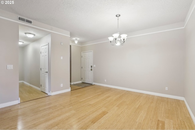 unfurnished room with a textured ceiling, visible vents, baseboards, light wood-style floors, and an inviting chandelier