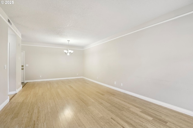 unfurnished room with light wood-type flooring, a notable chandelier, a textured ceiling, and baseboards