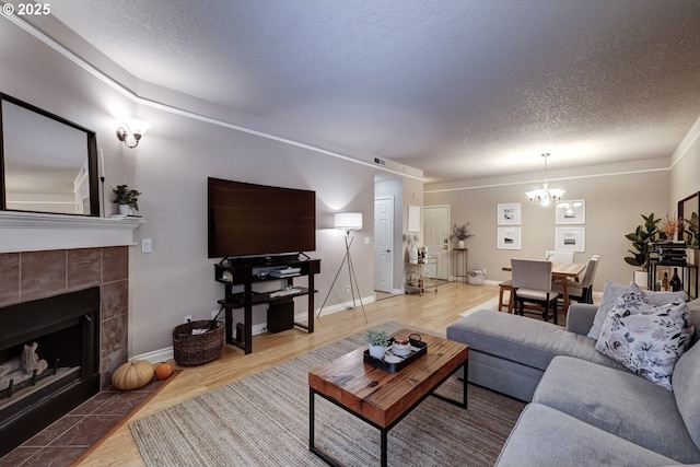 living room with hardwood / wood-style flooring, a notable chandelier, a tile fireplace, and a textured ceiling