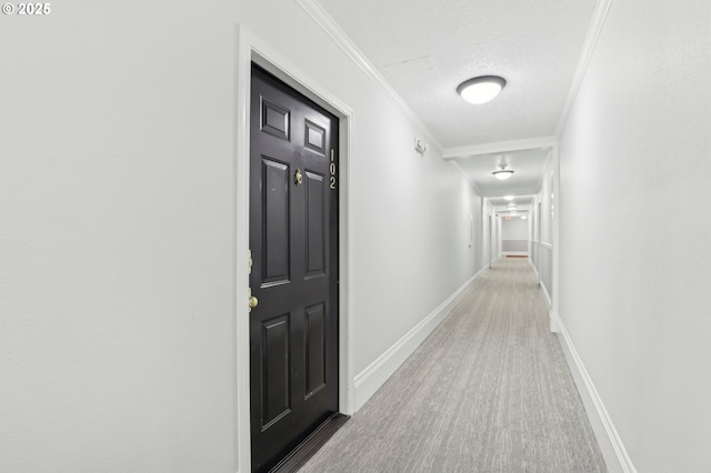 hallway with ornamental molding, a textured ceiling, baseboards, and wood finished floors