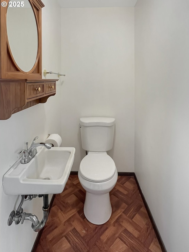 half bathroom with toilet, baseboards, and a sink