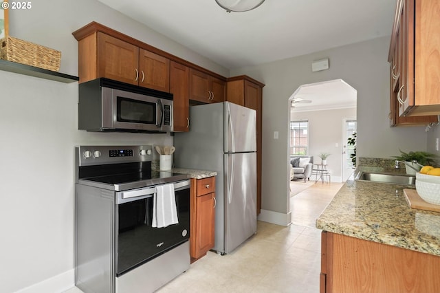 2643 NW Raleigh St Unit 30, Portland, OR 97210 - kitchen featuring stainless steel appliances, arched walkways, brown cabinetry, a sink, and baseboards