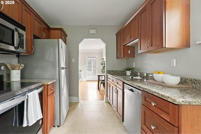 2643 NW Raleigh St Unit 30, Portland, OR 97210 - kitchen featuring stainless steel appliances, a sink, arched walkways, light tile patterned floors, and brown cabinets