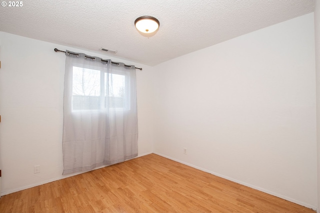 empty room featuring a textured ceiling, visible vents, light wood-style flooring, and baseboards