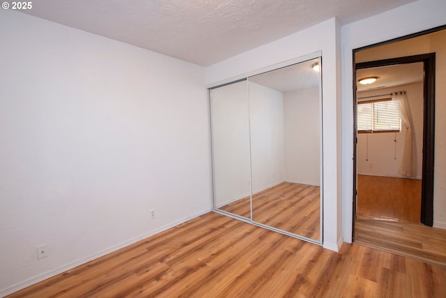 unfurnished bedroom featuring a textured ceiling, a closet, light wood-style flooring, and baseboards