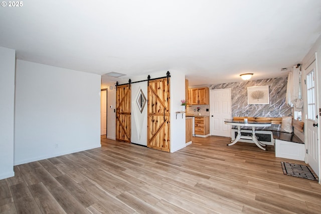 living area with light wood-type flooring, a barn door, and baseboards