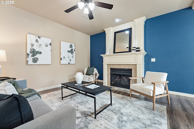 living area featuring a ceiling fan, a tile fireplace, baseboards, and wood finished floors