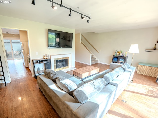 living room with stairway, wood finished floors, baseboards, a fireplace with flush hearth, and track lighting