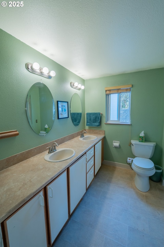 full bathroom with double vanity, a textured ceiling, toilet, and a sink