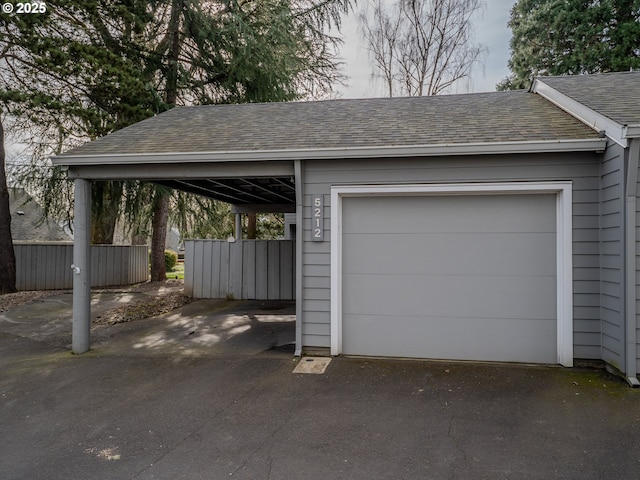 garage with aphalt driveway, a carport, and fence