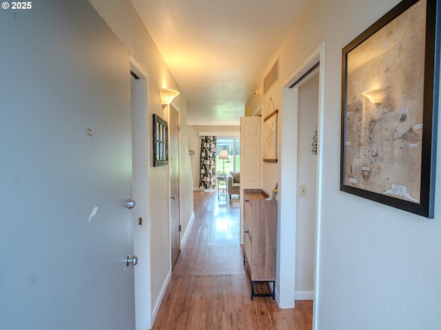 hall featuring light wood-style flooring, visible vents, and baseboards