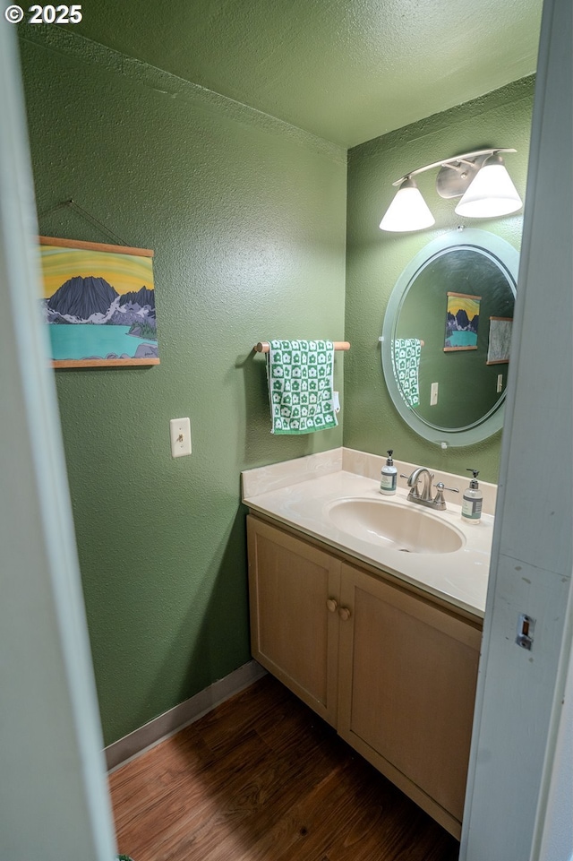 bathroom with baseboards, wood finished floors, vanity, and a textured wall