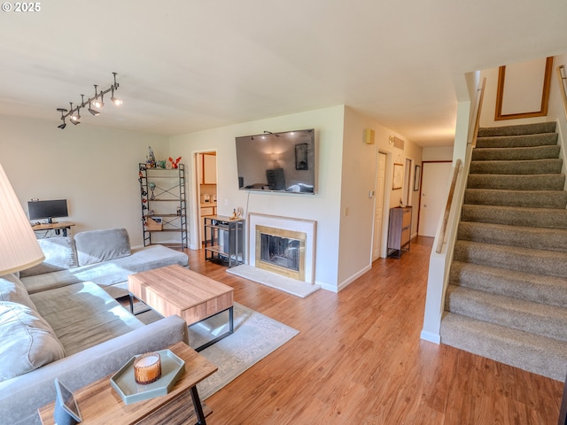 living room with baseboards, stairs, track lighting, light wood-style floors, and a glass covered fireplace