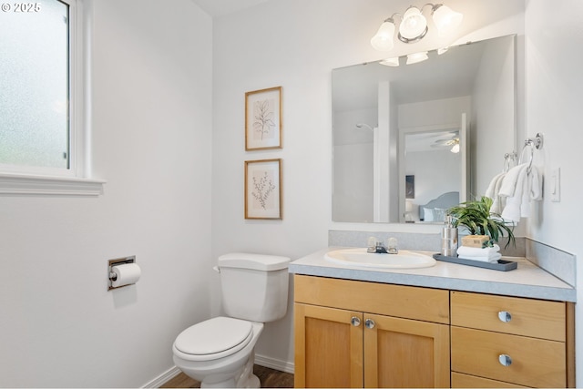 bathroom with toilet, vanity, a ceiling fan, baseboards, and wood finished floors
