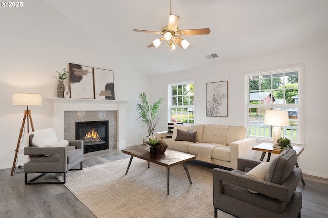 living area with wood finished floors, a ceiling fan, baseboards, a tiled fireplace, and vaulted ceiling