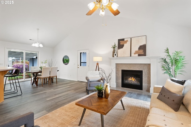 living room featuring high vaulted ceiling, wood finished floors, a fireplace with flush hearth, a chandelier, and ceiling fan