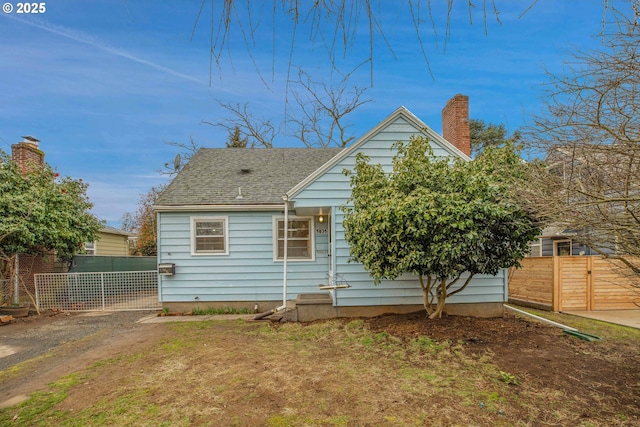 rear view of house featuring entry steps, roof with shingles, fence, and a chimney