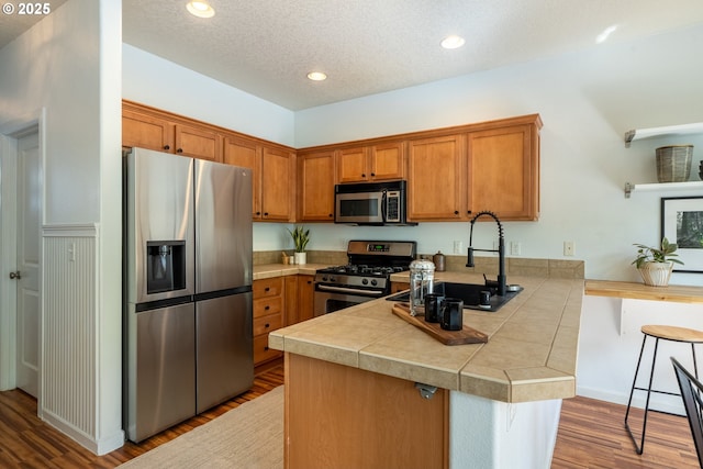 12115 NE 40th Cir, Vancouver, WA 98682 - kitchen featuring a peninsula, a sink, wood finished floors, brown cabinetry, and appliances with stainless steel finishes
