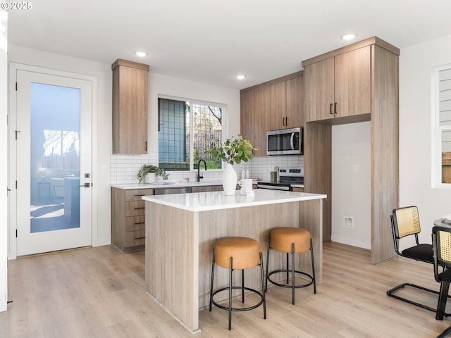 kitchen with appliances with stainless steel finishes, a center island, a breakfast bar area, and light hardwood / wood-style flooring